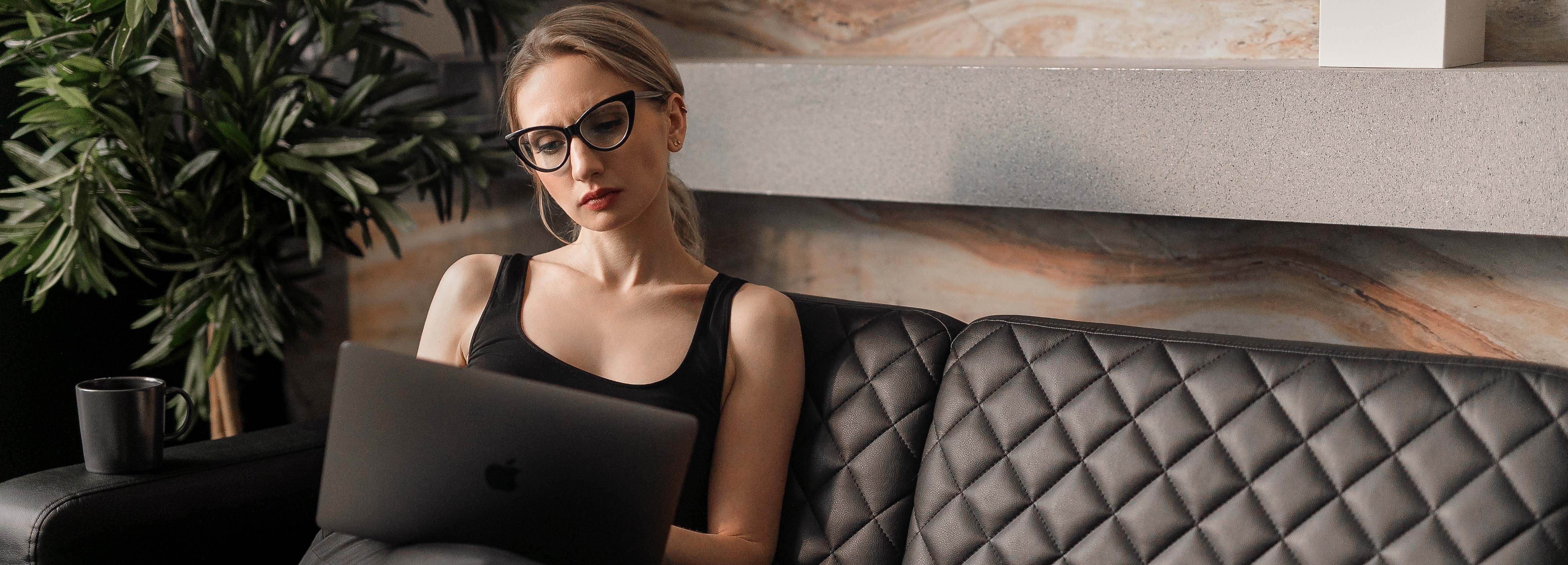 mujer en camiseta negra con gafas sentada en un sofá de cuero negro